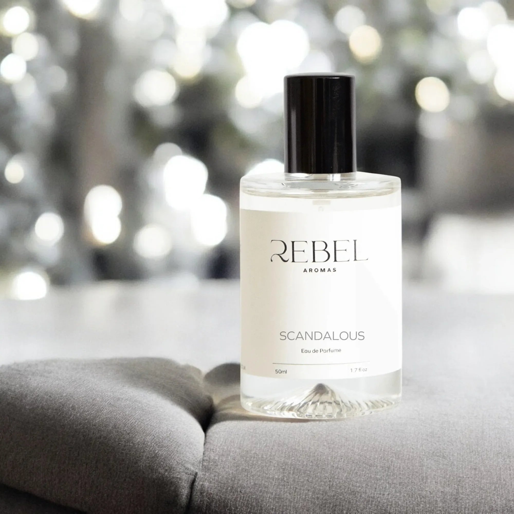 Perfume bottle labeled 'REBEL AROMAS' on a gray surface with a blurred light background
