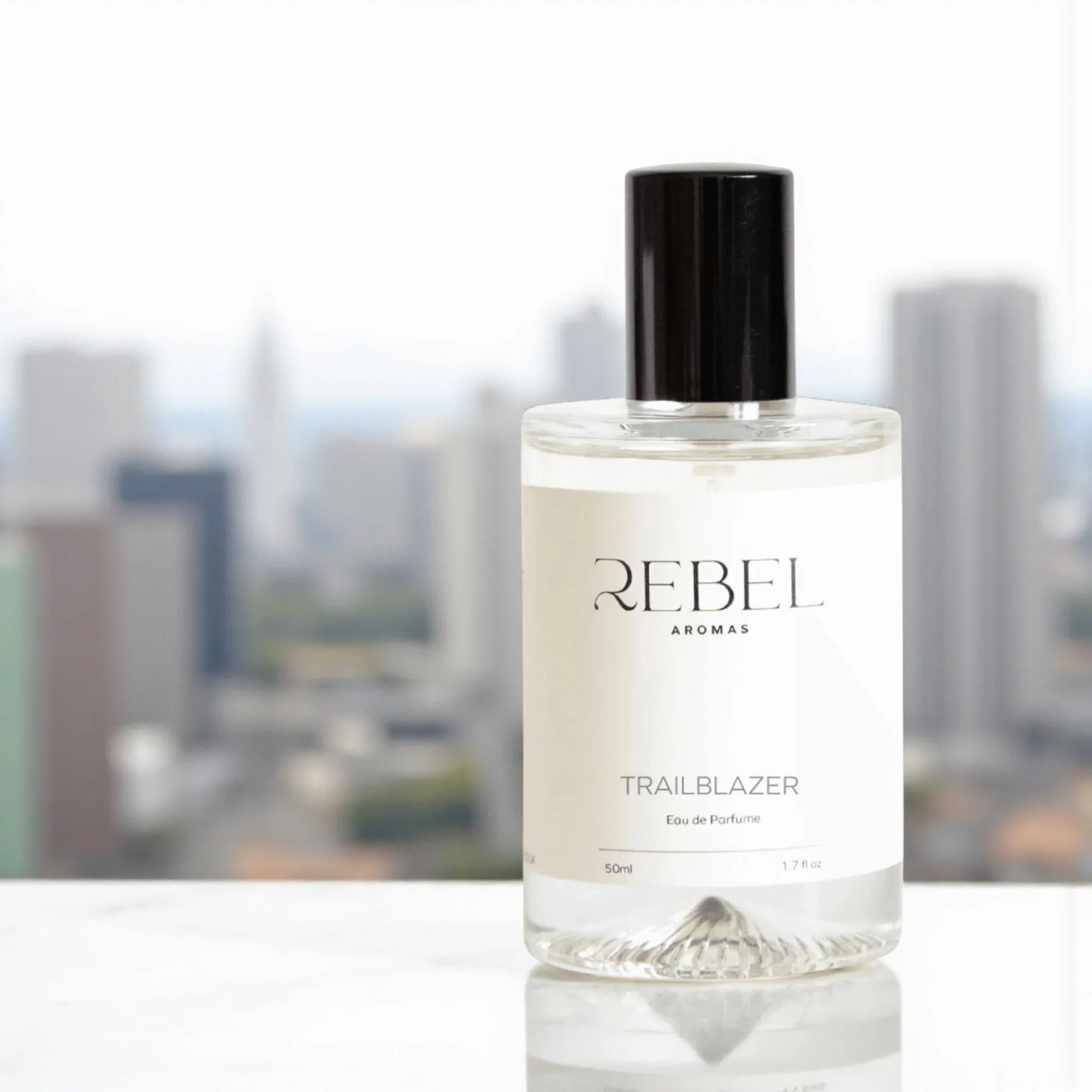 Bottle of Rebel Aromas Trailblazer perfume with a cityscape in the background