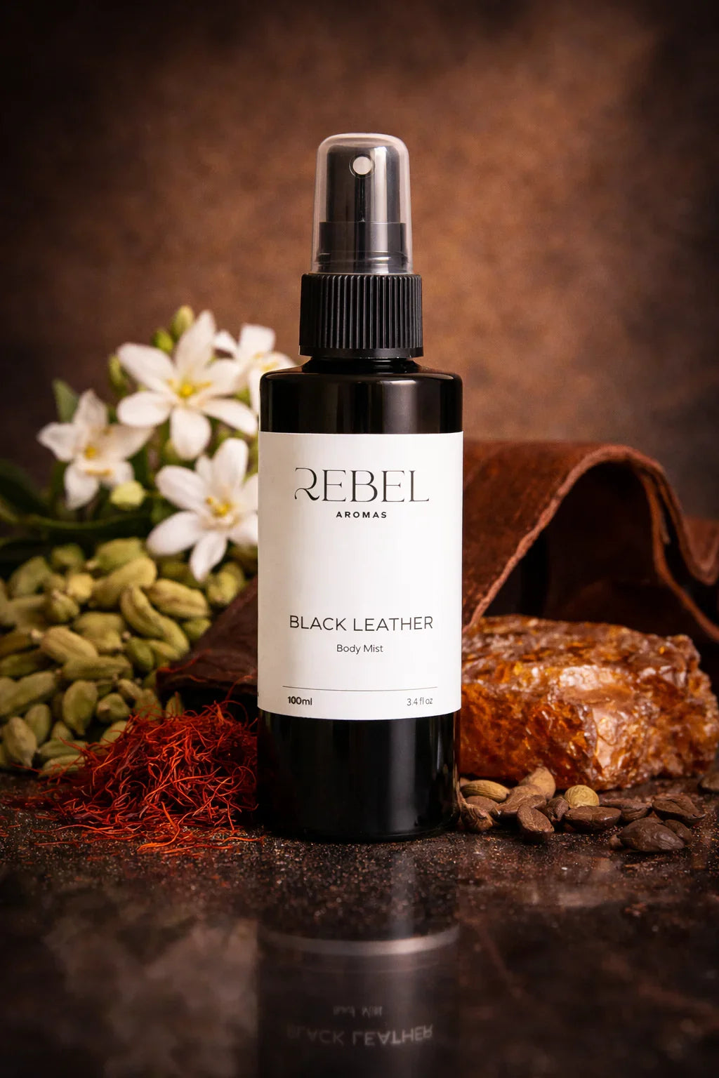 Black leather body mist bottle labeled 'REBEL' with flowers and a leather pouch in the background.