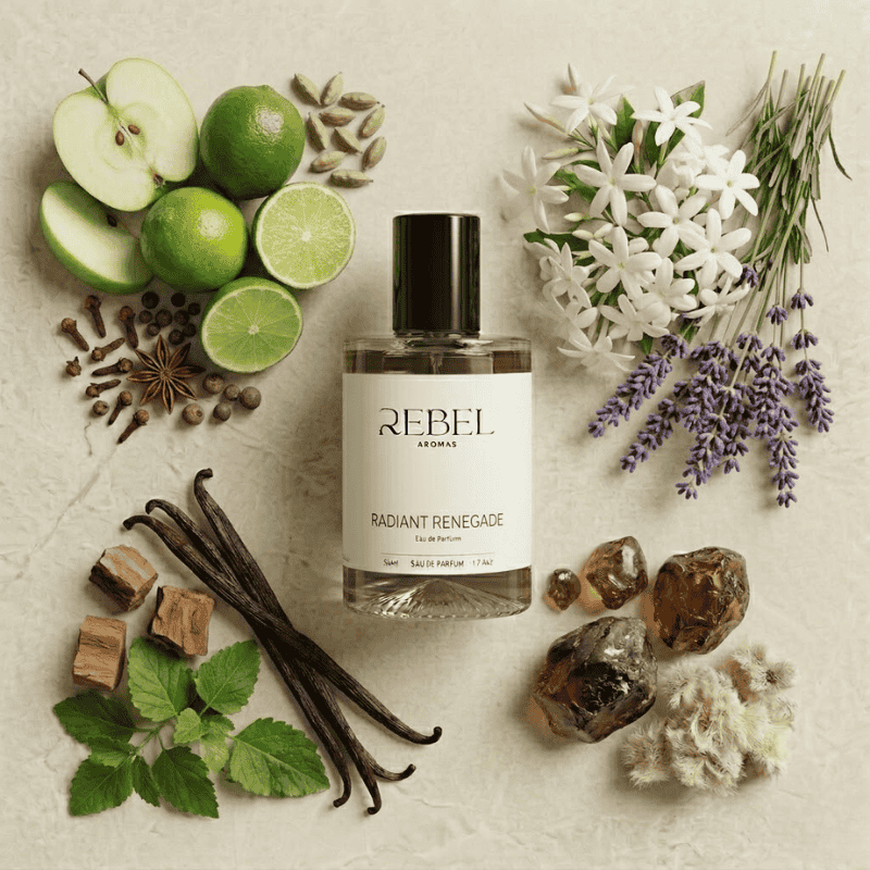 Rebel Aromas perfume bottle surrounded by natural elements like fruits, flowers, and herbs on a textured surface.